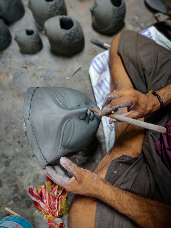 A detailed close-up of an artisan shaping a clay mask by hand in a workshop.