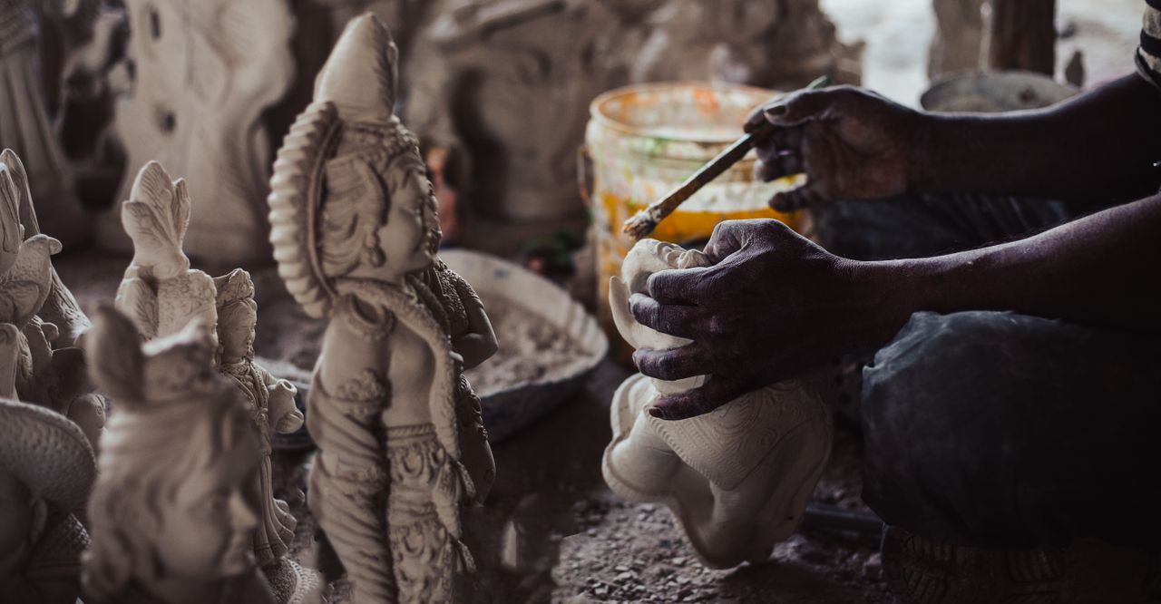 Close-up of artisan crafting a detailed Buddha figurine in a workshop, showcasing intricate artistry.