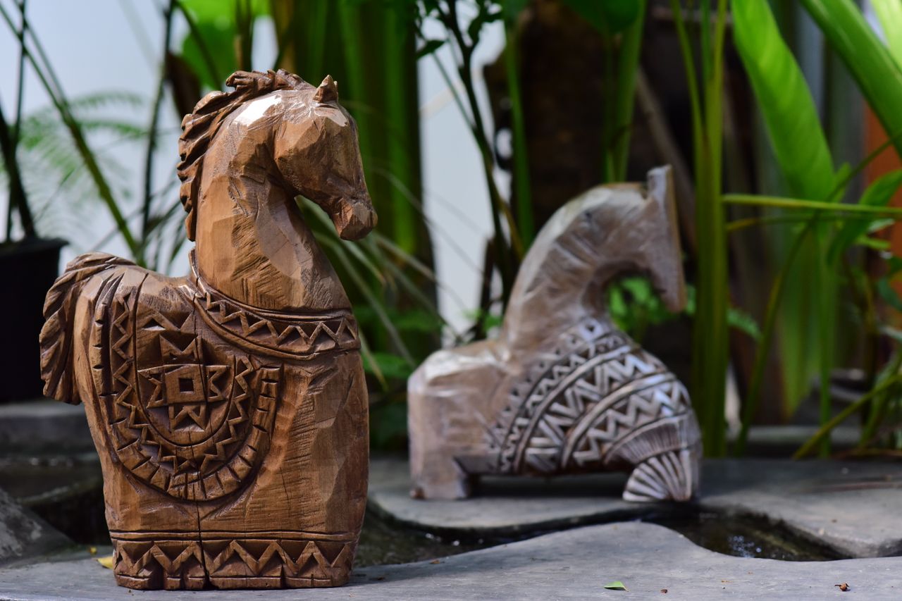 Wooden horse sculptures with detailed carvings displayed outdoors amidst lush greenery.