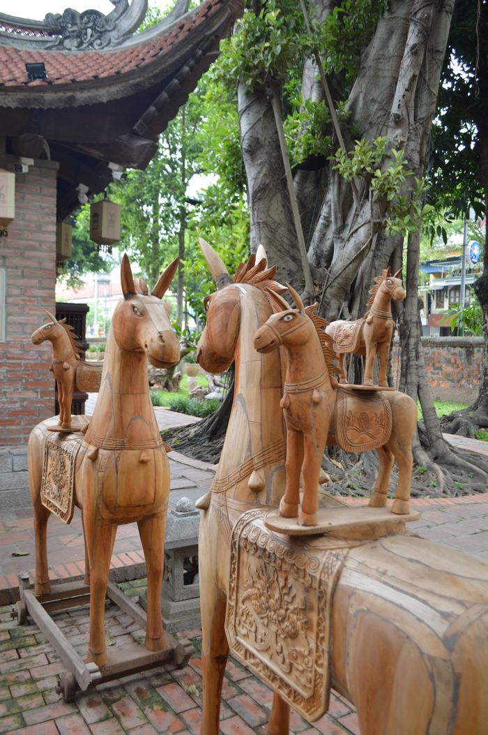 Intricate wooden horse sculptures displayed outdoors in a garden setting, showcasing cultural craftsmanship.