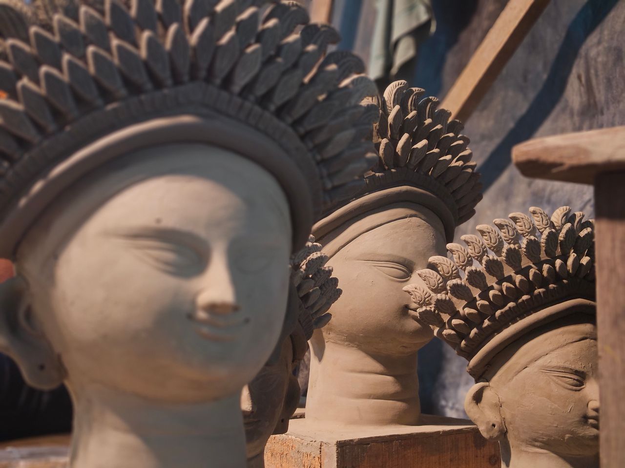 Clay sculptures with intricate headpieces illuminated in natural light.